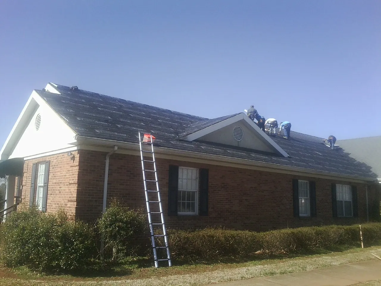 Crew tearing shingles off a brick ranch roof with a ladder set — Metal Roof Repair work by our crew in Orangeville