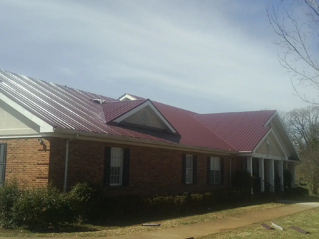 Red metal roof with gabled entries on a long brick building, from a Hail Damage Roof Repair job in Orangeville