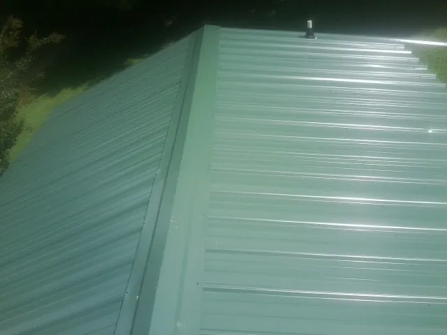 New green metal panels meeting at the ridge of a roof — Flat Roof Repair work by our crew in Orangeville