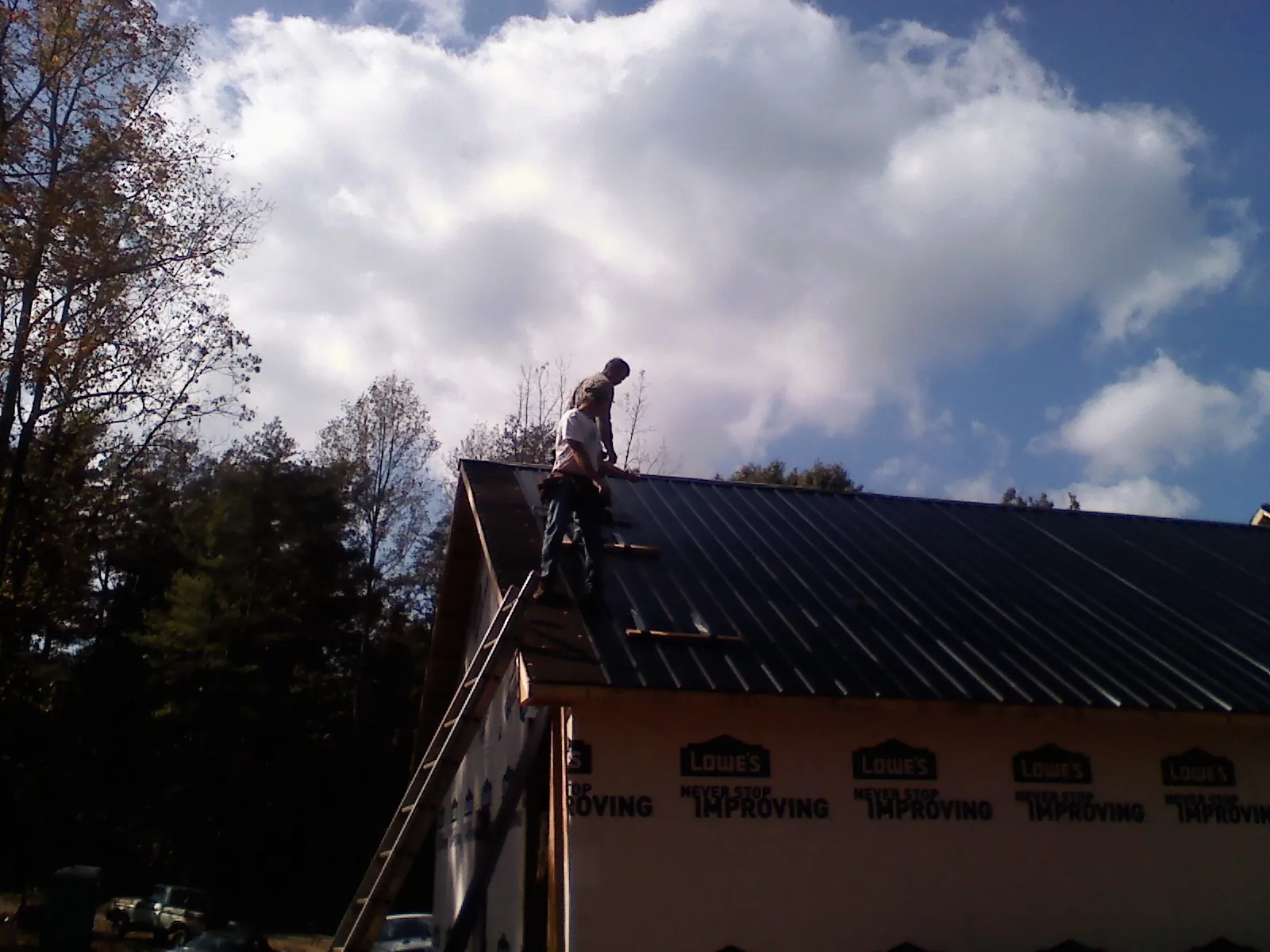 Roofer fastening dark metal panels high against a cloudy sky, from a Roof Inspection job in Orangeville