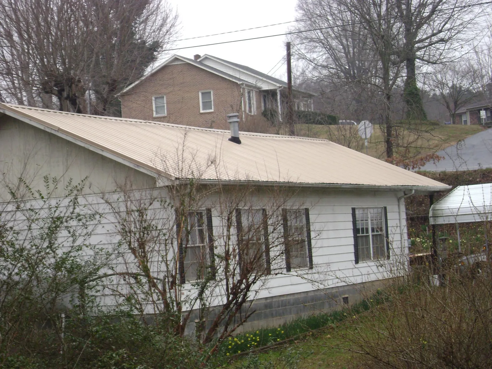 Tan metal roof on a white sided house set into a hillside — Commercial Roofing by Roofing Brothers in Orangeville