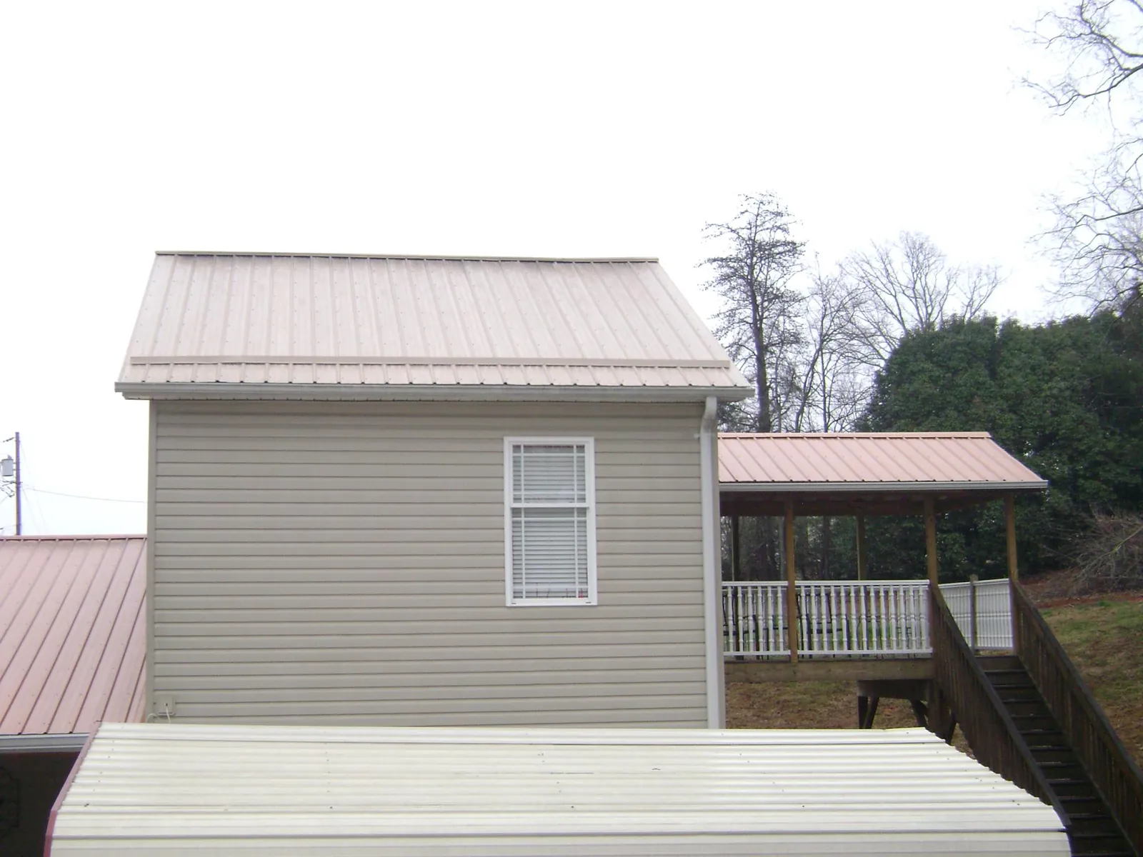 Tan metal roofs on a two story addition and attached porch, from a Roof Replacement job in Orangeville